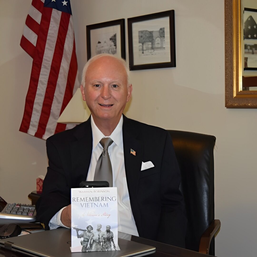 A man sitting at a desk in front of an american flag.